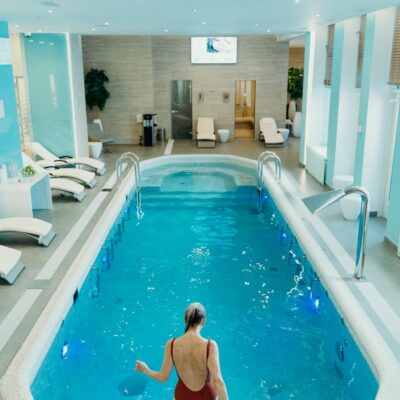 A serene indoor swimming pool setting with a woman in a red swimsuit stepping in.