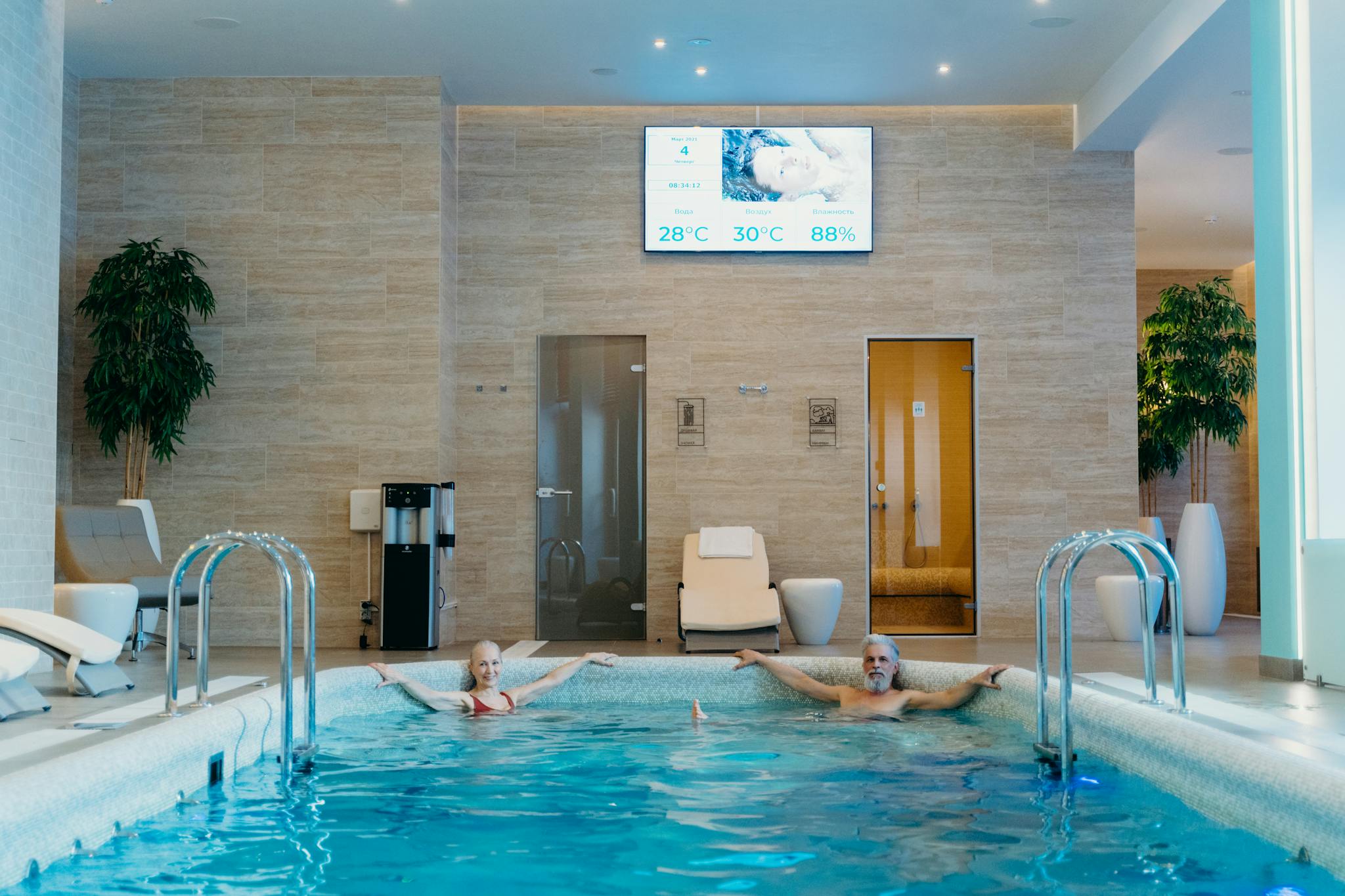 Two adults enjoying leisure time at an indoor swimming pool with spa-like ambiance.